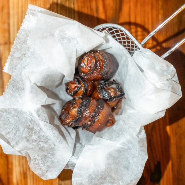 Bacon-wrapped dates, a popular American appetizer, served in a metal basket lined with white paper.