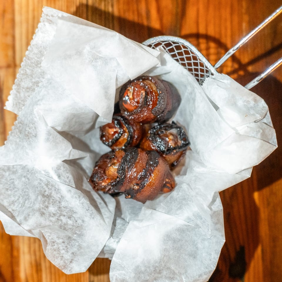 Bacon-wrapped dates, a popular American appetizer, served in a metal basket lined with white paper.