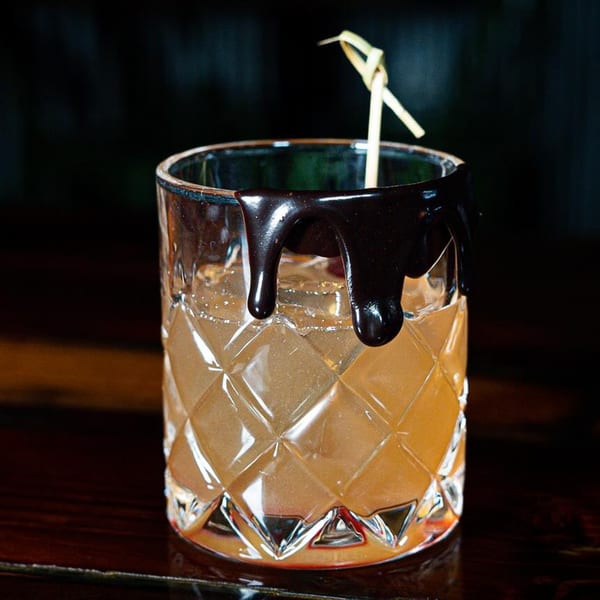 A Girl in the Park cocktail in a diamond-patterned glass with chocolate syrup dripping down the rim.
