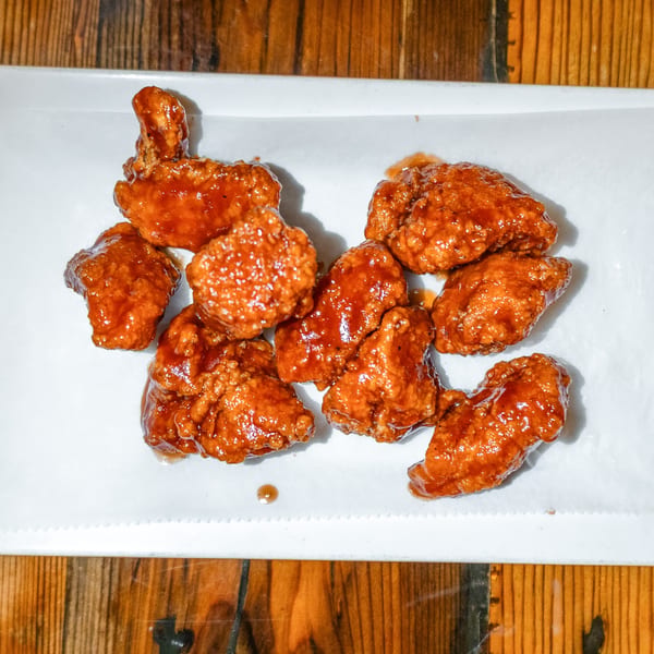 Girl in the Park's boneless chicken wings, coated in a glistening orange-brown sauce, on white paper.