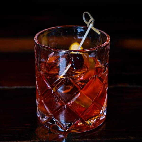 A Girl in the Park Old Fashioned cocktail with a cherry and orange peel garnish.