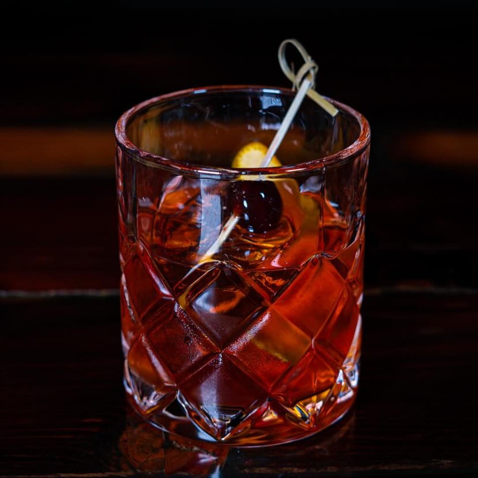 A Girl in the Park Old Fashioned cocktail with a cherry and orange peel garnish.