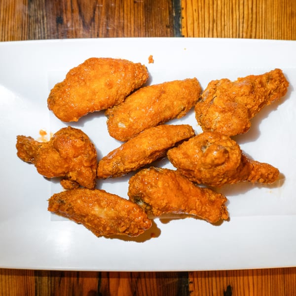 A white rectangular plate filled with golden-brown, saucy chicken wings on a wooden table.