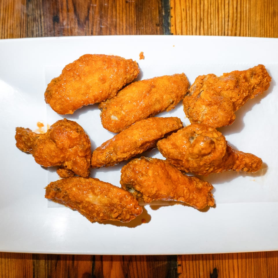 A white rectangular plate filled with golden-brown, saucy chicken wings on a wooden table.