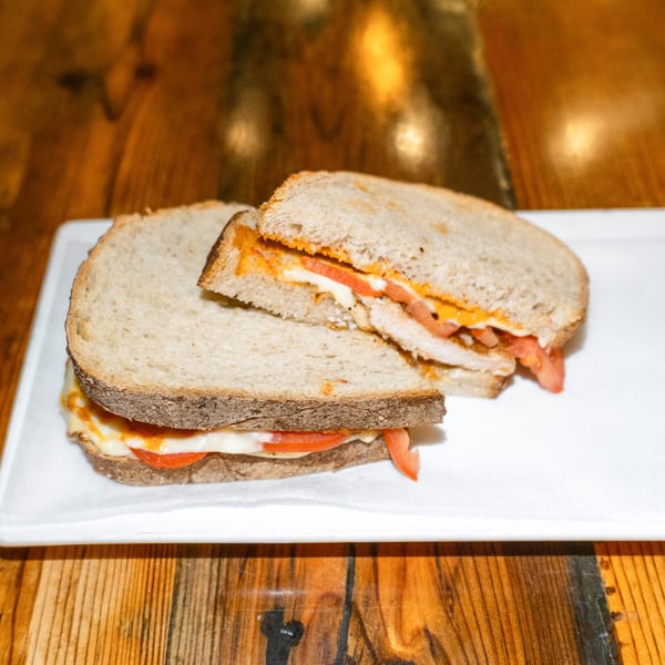 A grilled chicken sandwich with melted cheese and sliced tomatoes on toasted bread.