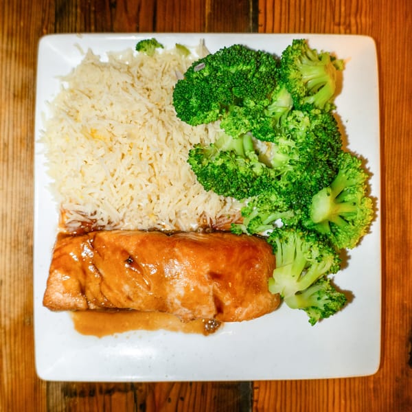 Girl in the Park's salmon with a rich sauce, rice, and bright green broccoli on a white plate.