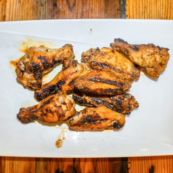 A white rectangular plate filled with several grilled chicken wings, some with visible char marks.