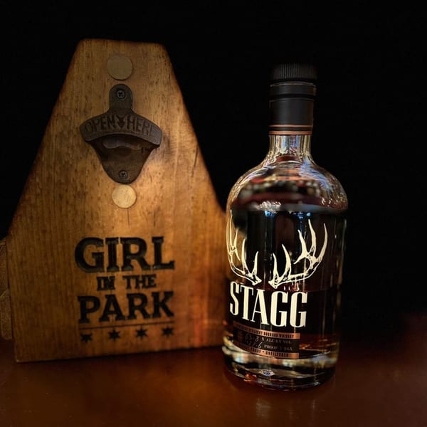 A bottle of Stagg bourbon whiskey next to a wooden Girl in the Park bottle opener.