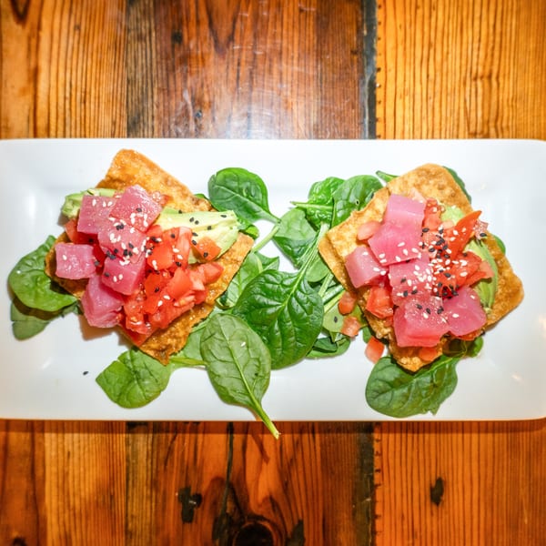 Two tuna poke wonton tacos with avocado, tomatoes, and spinach on a white plate.