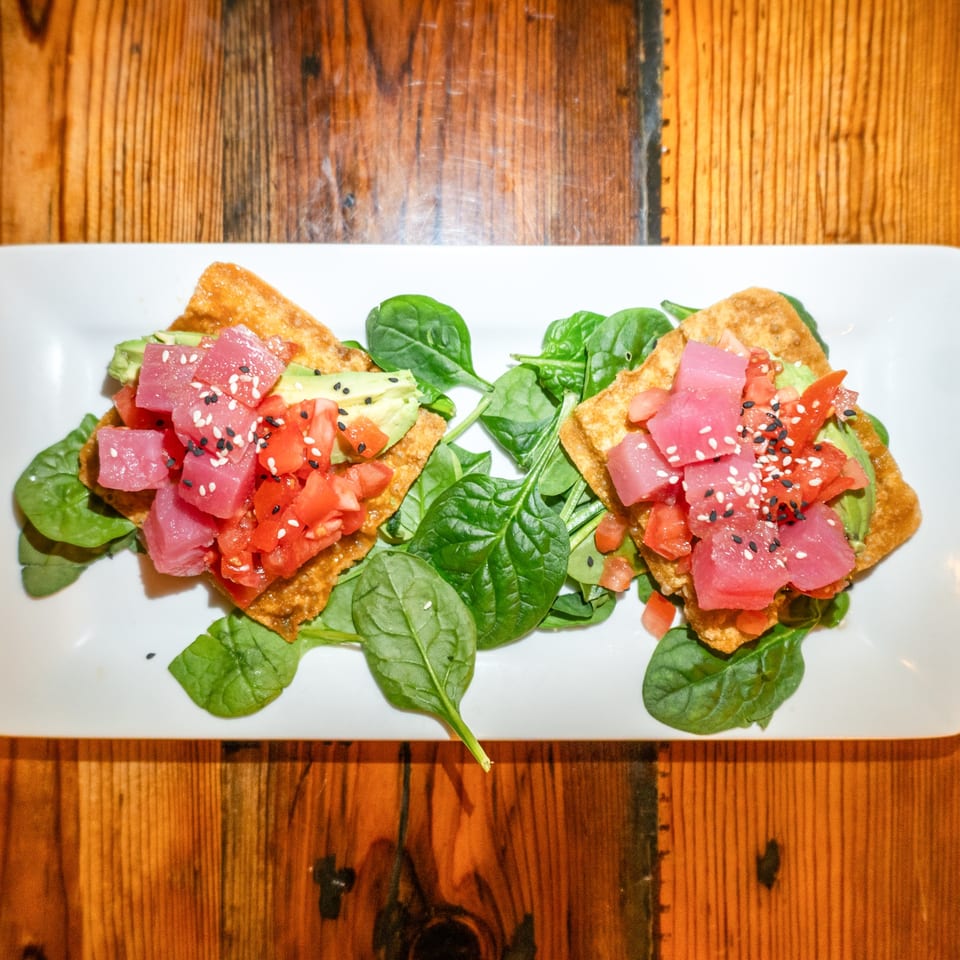 Two tuna poke wonton tacos with avocado, tomatoes, and spinach on a white plate.