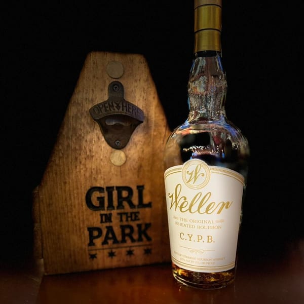 A bottle of Weller bourbon next to a wooden bottle opener with "Girl in the Park" logo.