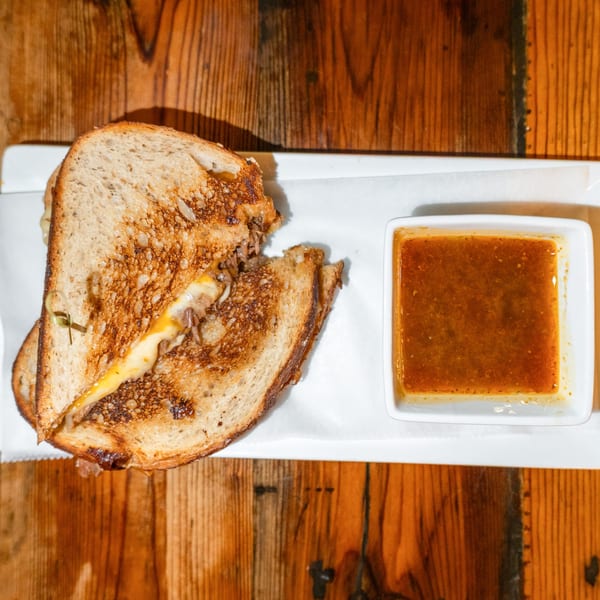 A grilled cheese sandwich with melted cheese and caramelized onions, served with a side of dipping sauce.