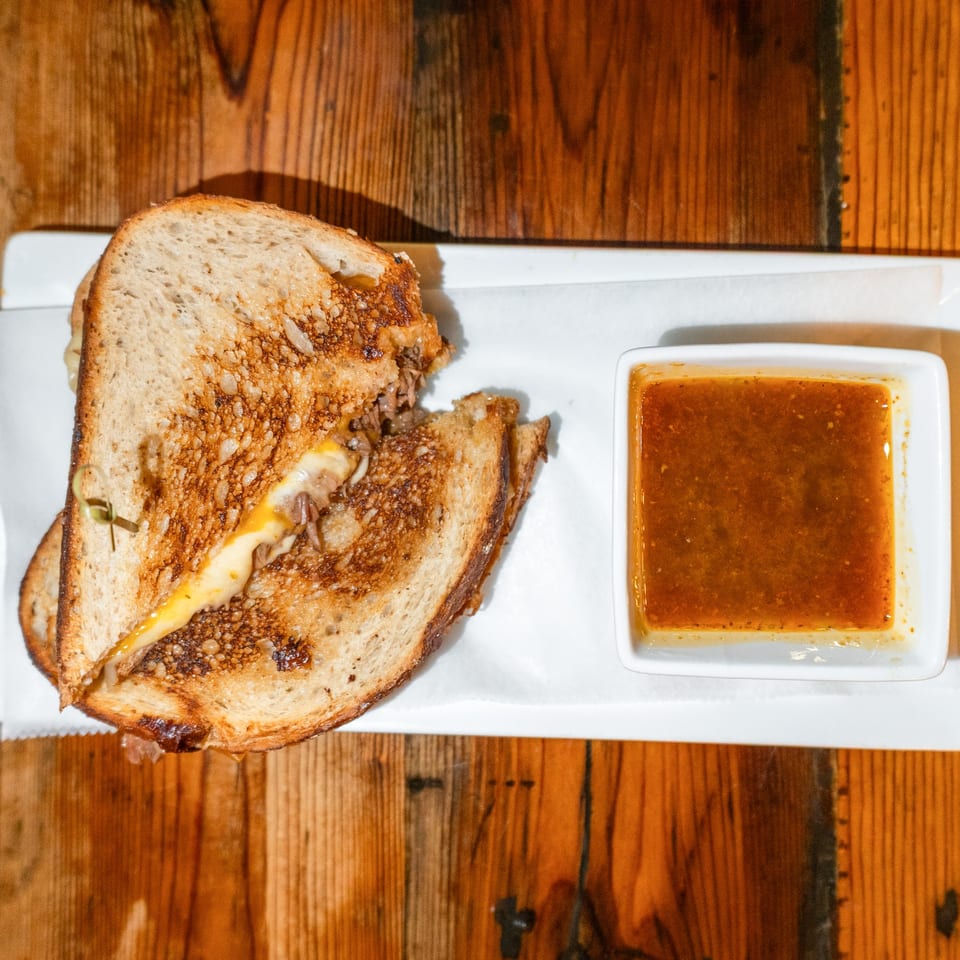 A grilled cheese sandwich with melted cheese and caramelized onions, served with a side of dipping sauce.