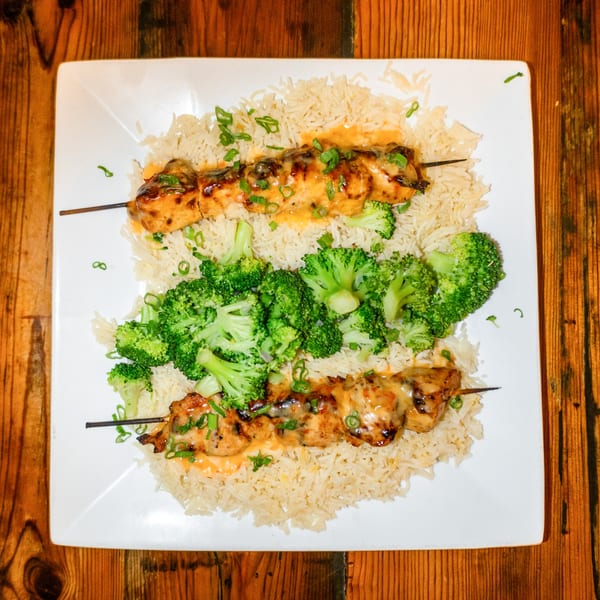 Two chicken skewers with sauce and scallions, served on a bed of rice with broccoli.
