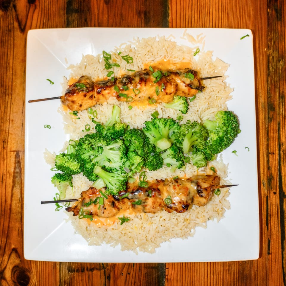Two chicken skewers with sauce and scallions, served on a bed of rice with broccoli.